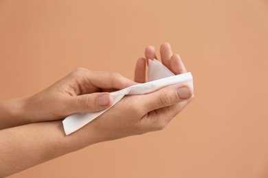 Photo of Woman cleaning hands with paper tissue on light brown background, closeup