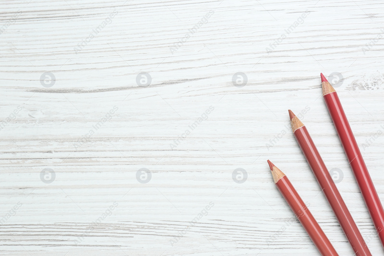 Photo of Lip pencils on white wooden table, flat lay. Space for text