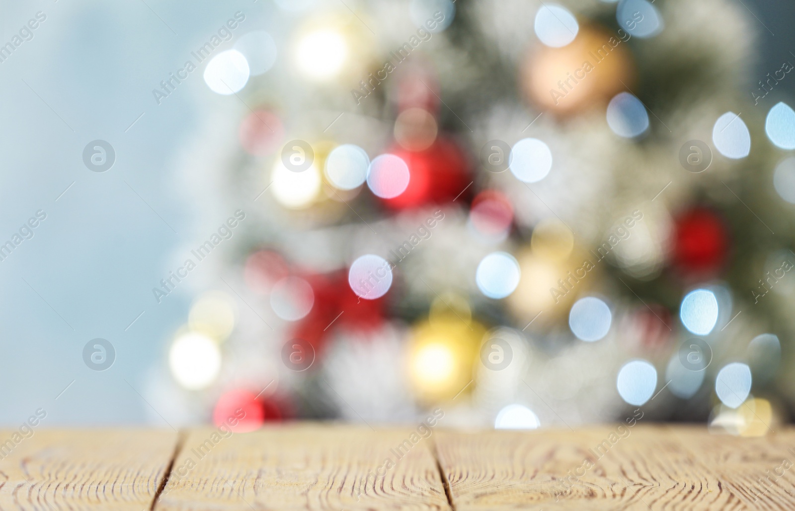 Photo of Empty white wooden table and blurred fir tree with Christmas lights on background, bokeh effect. Space for design