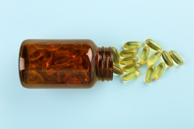 Bottle and vitamin capsules on light blue background, top view