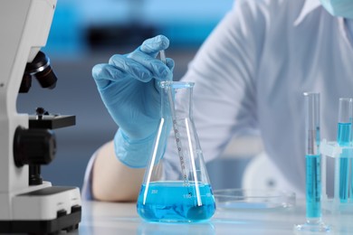 Scientist taking sample of light blue liquid, closeup