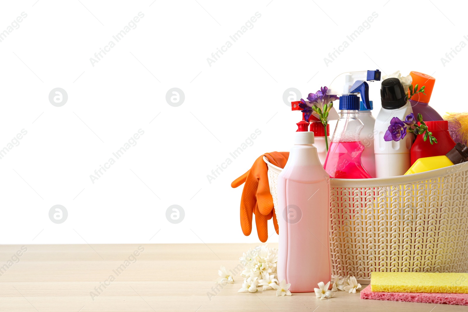 Photo of Plastic basket with spring flowers and cleaning supplies on wooden table. Space for text