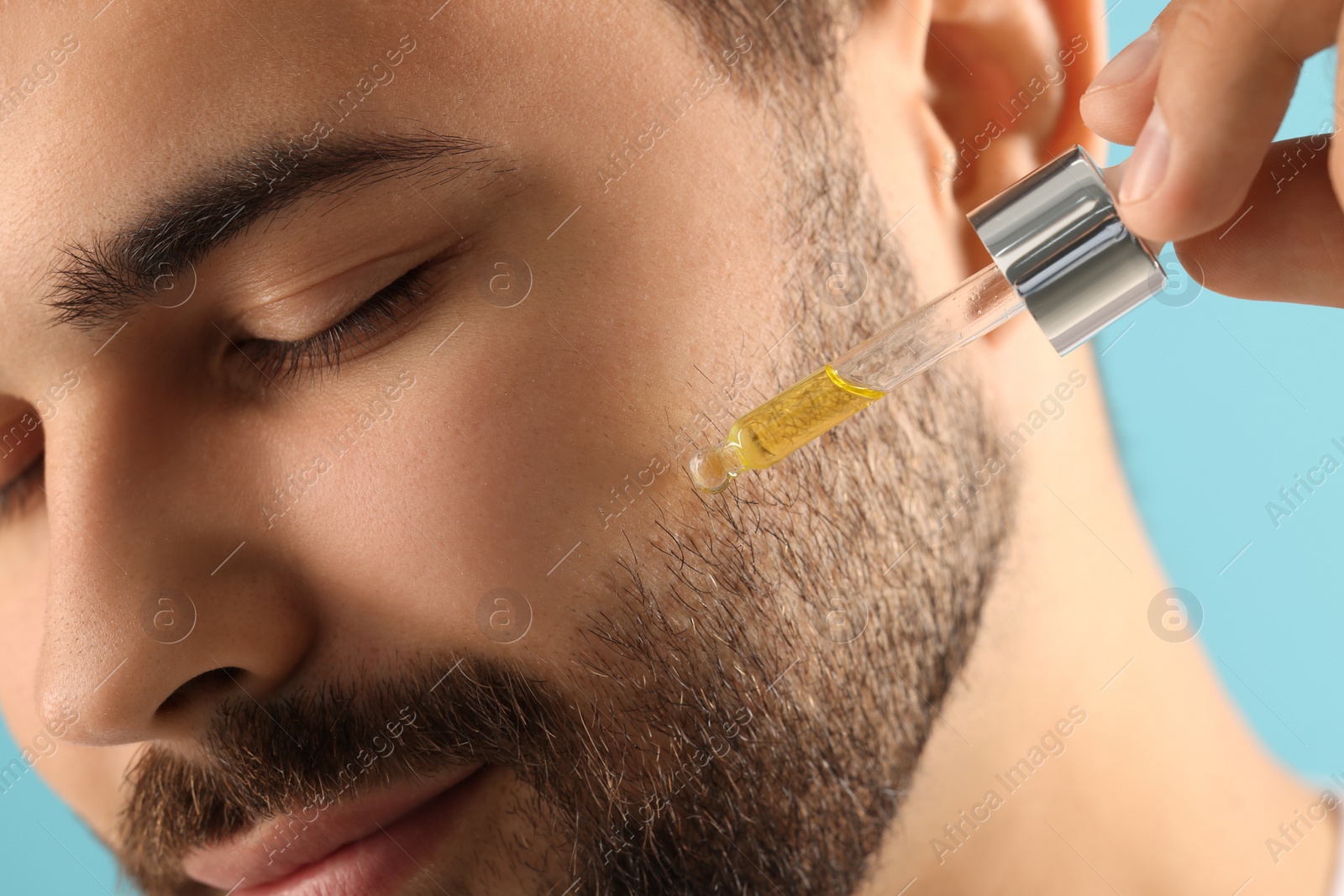 Photo of Handsome man applying cosmetic serum onto face, closeup