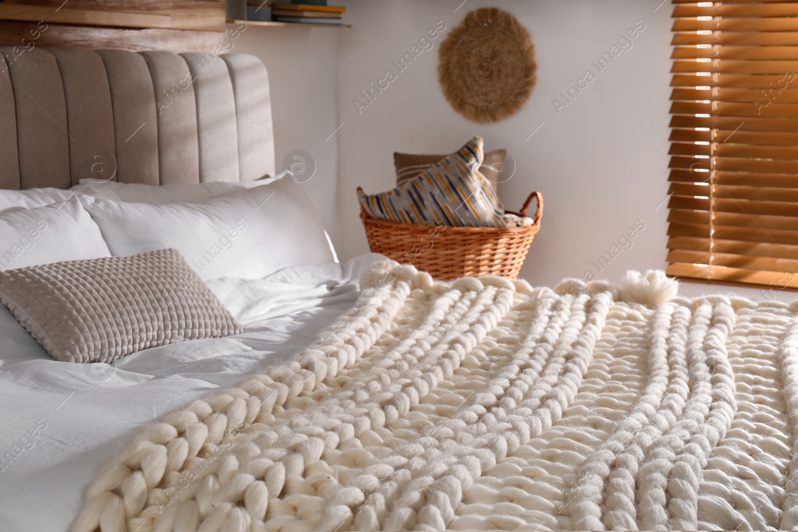 Photo of Bed with white knitted plaid indoors. Interior design