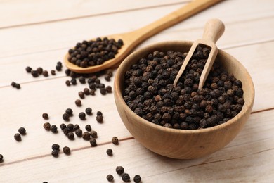 Photo of Aromatic spice. Black peppercorns and scoop in bowl on wooden table