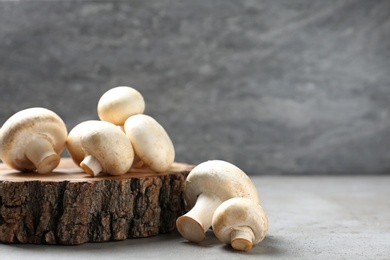 Photo of Fresh champignon mushrooms with wooden stump on table, space for text