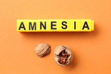 Word Amnesia made of yellow cubes and broken walnut on orange background, flat lay