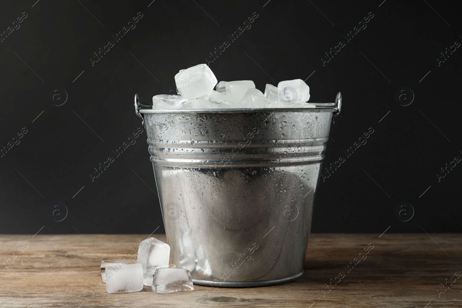 Photo of Metal bucket with ice cubes on wooden table