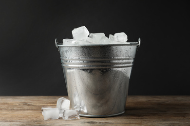 Photo of Metal bucket with ice cubes on wooden table