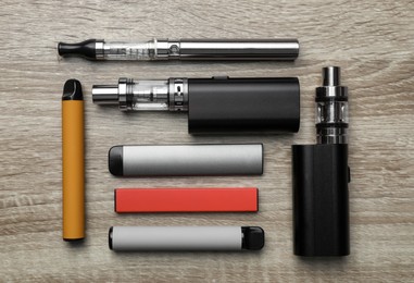 Photo of Different electronic cigarettes on wooden background, flat lay