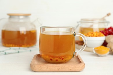 Photo of Glass cup of immunity boosting tea with ingredients on white wooden table
