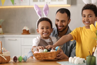 Happy African American father and his cute children with Easter eggs at table in kitchen