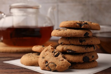 Photo of Stack of delicious chocolate chip cookies and tea on wooden table, closeup. Space for text