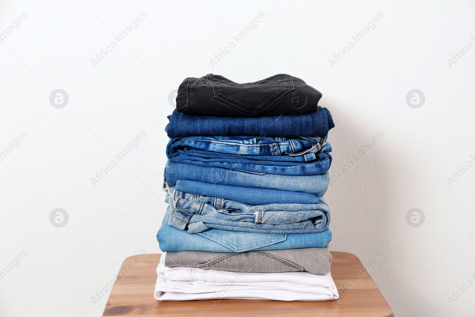 Photo of Stack of different jeans on table against white background