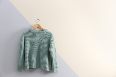 Photo of Hanger with stylish sweater on color wall. Space for text