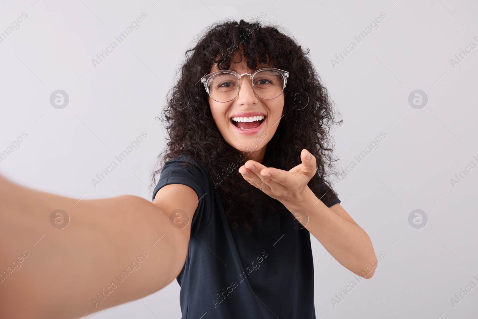 Photo of Beautiful young woman in eyeglasses taking selfie on light grey background