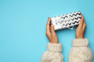 Young woman holding Christmas gift on light blue background, top view. Space for text