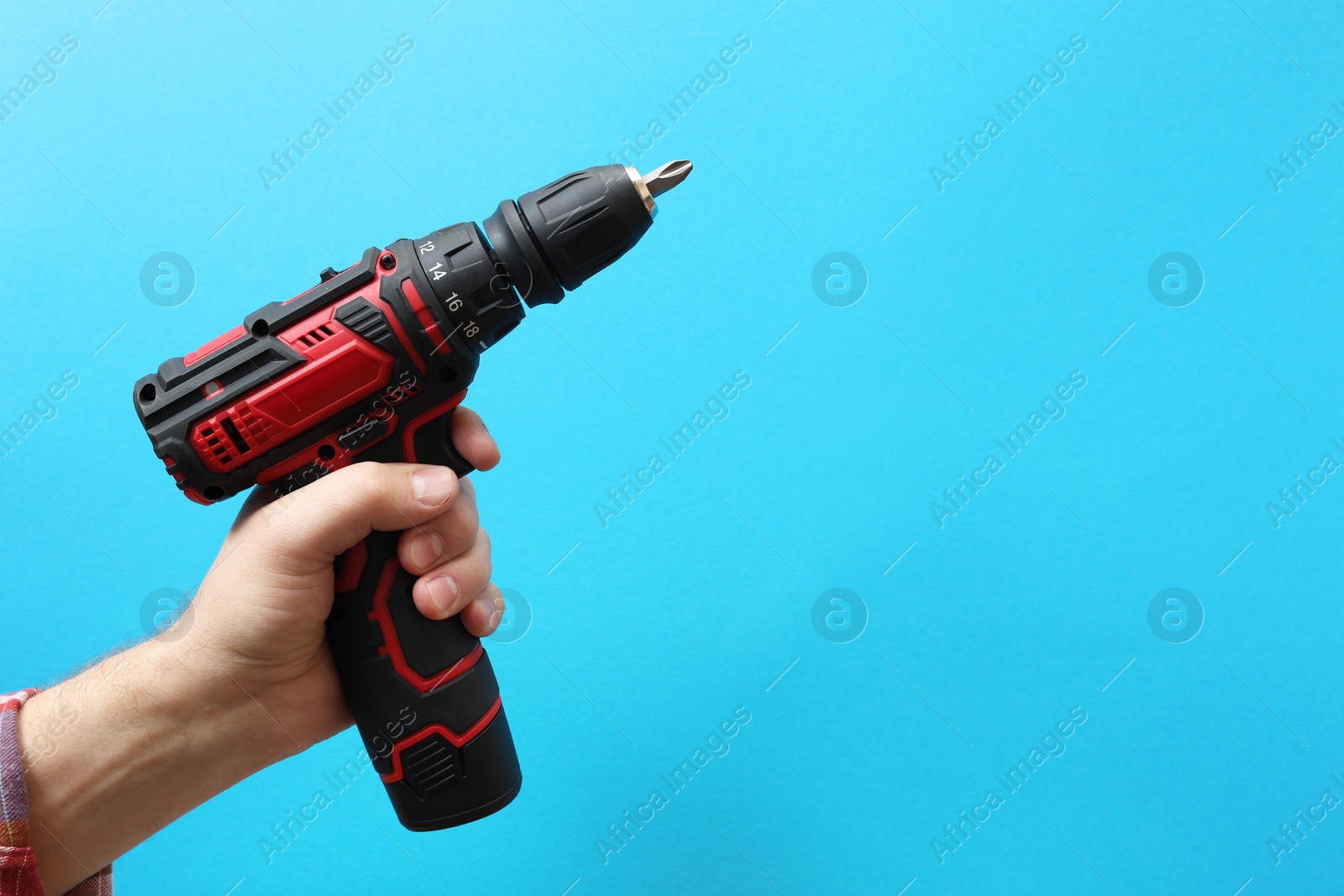 Photo of Handyman holding electric screwdriver on light blue background, closeup. Space for text