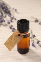 Bottle of essential oil and lavender flowers on white wooden table, closeup