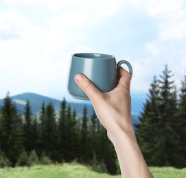 Image of Closeness to nature. Woman holding cup in mountains, closeup