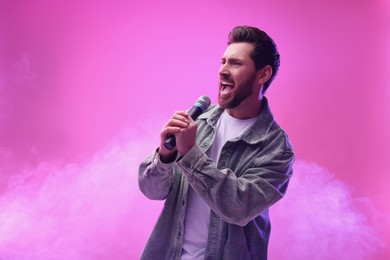 Photo of Handsome man with microphone singing on pink background. Space for text