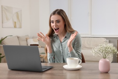 Photo of Surprised woman with laptop at wooden table in room