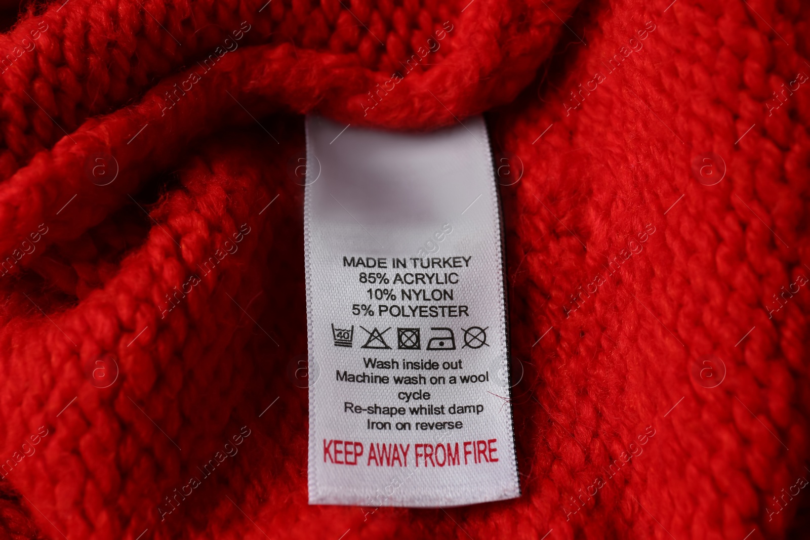 Photo of Clothing label with care symbols and material content on red sweater, closeup view