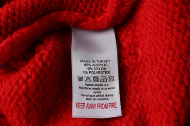 Clothing label with care symbols and material content on red sweater, closeup view