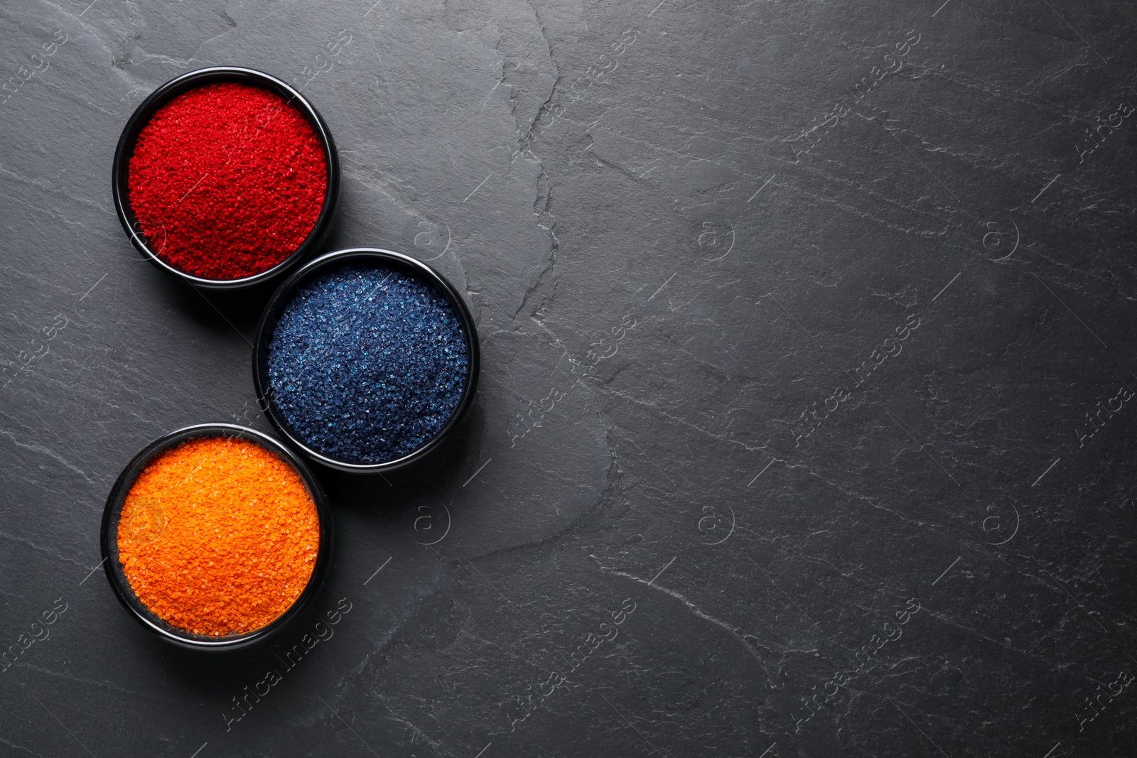 Photo of Bowls of different food coloring on grey table, flat lay. Space for text