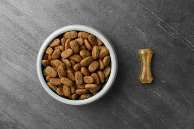 Photo of Dry dog food and treat (chew bone) on textured background, flat lay