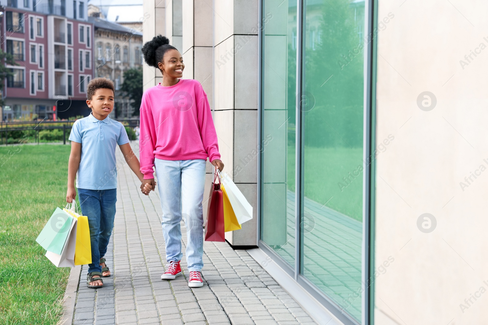 Photo of Family shopping. Happy mother and son with colorful bags near mall outdoors