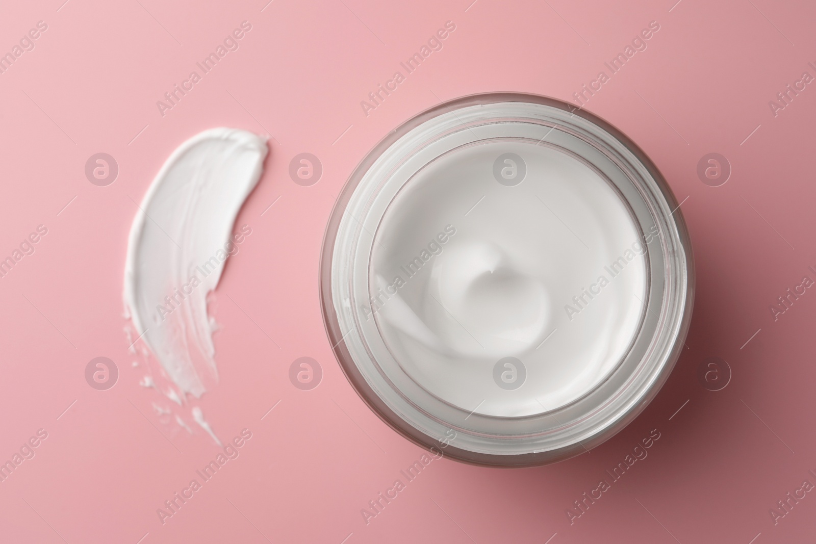 Photo of Jar of face cream and sample on pink background, top view