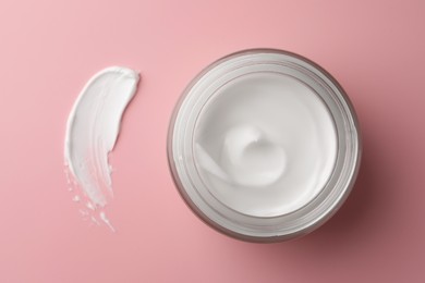 Jar of face cream and sample on pink background, top view