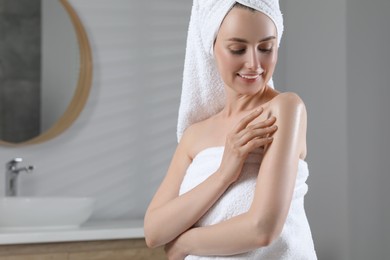 Photo of Happy woman applying body oil onto arm in bathroom, space for text