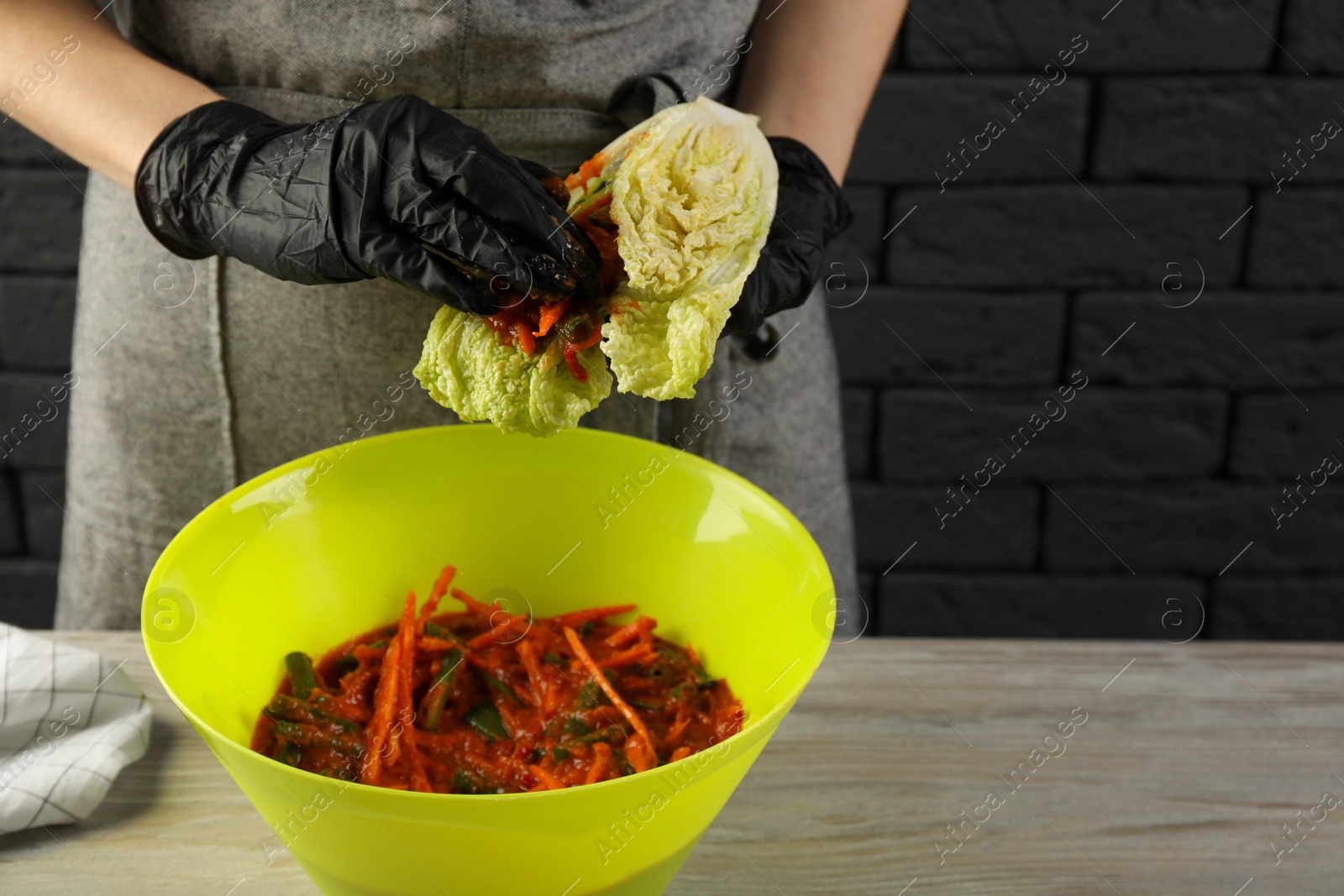 Photo of Woman preparing spicy cabbage kimchi at wooden table indoors, closeup