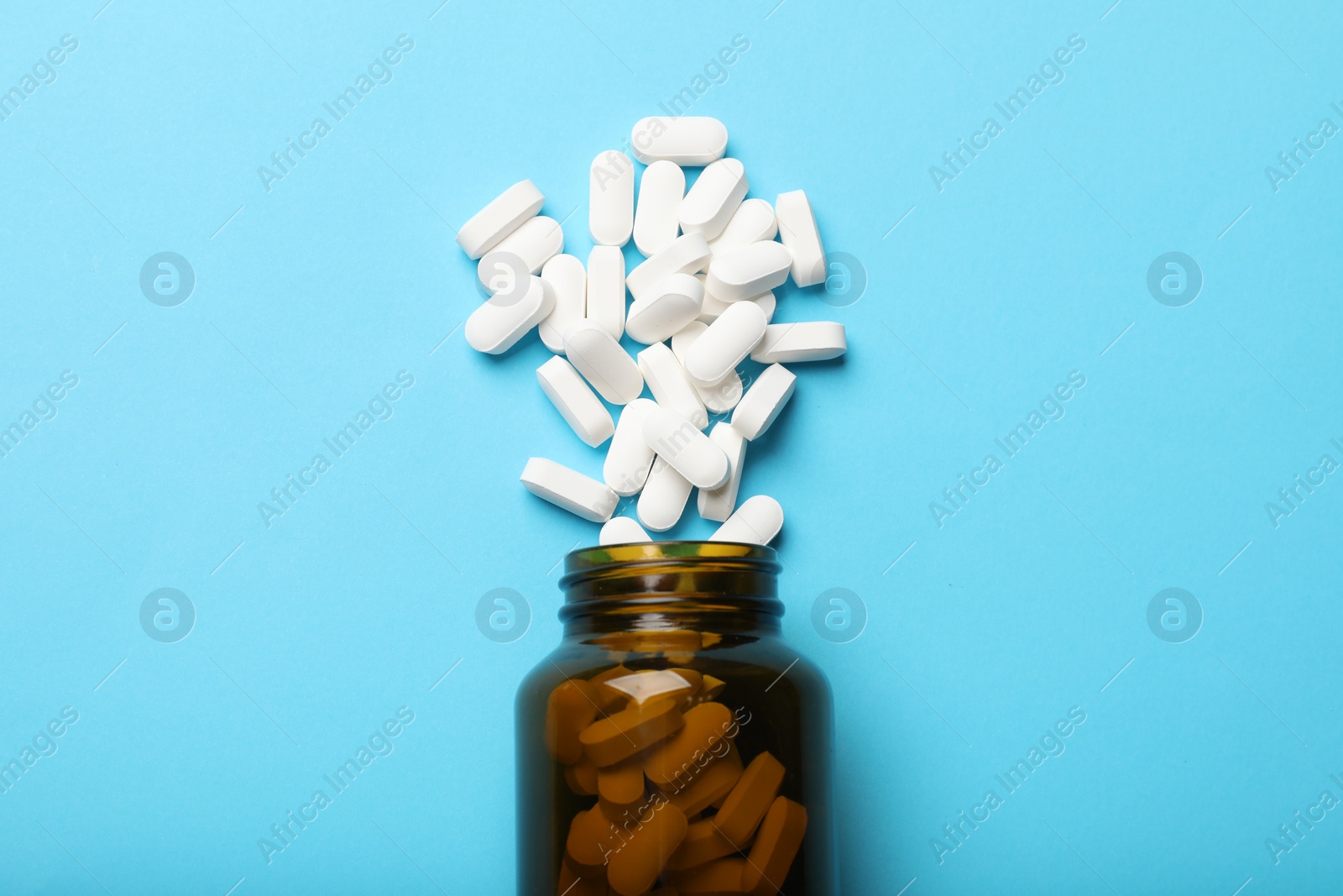 Photo of Bottle and vitamin capsules on light blue background, top view