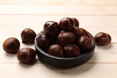Photo of Plate with roasted edible sweet chestnuts on wooden table, closeup