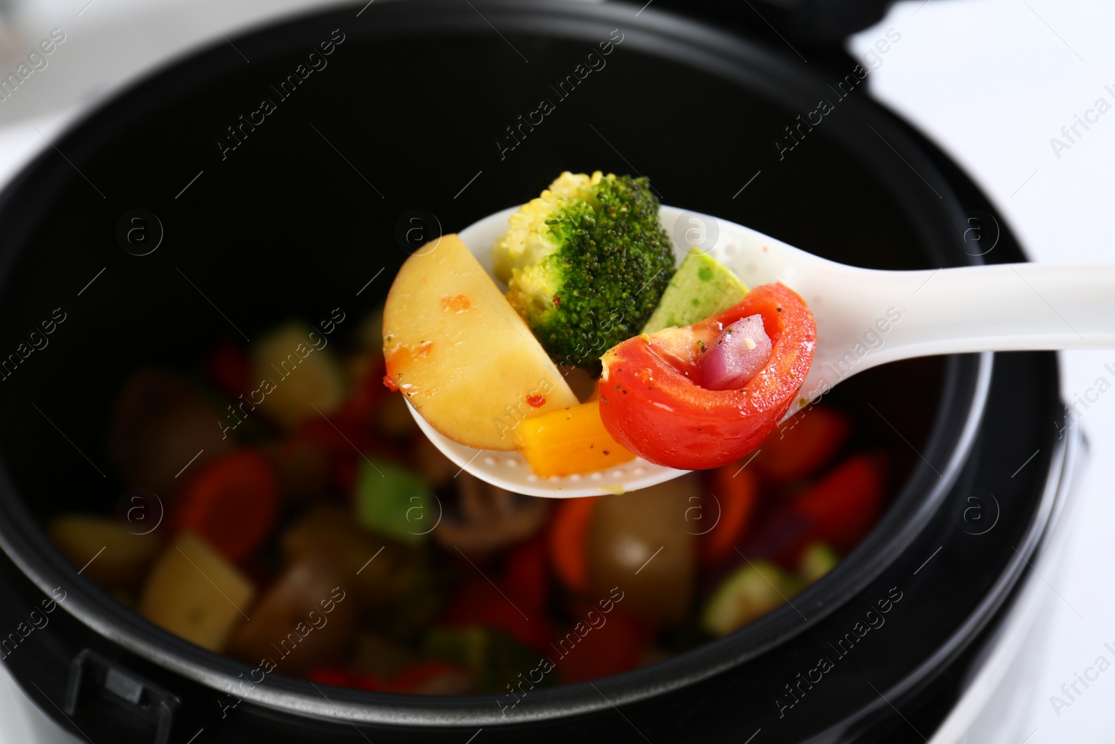 Photo of Spoon with vegetables over modern multi cooker, closeup