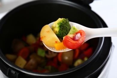 Spoon with vegetables over modern multi cooker, closeup