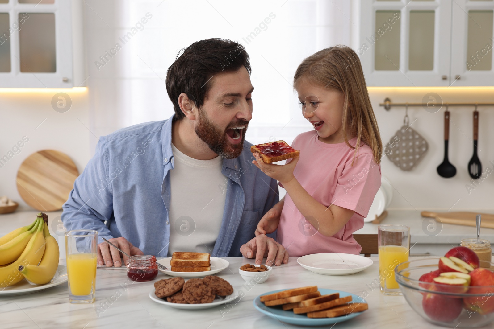 Photo of Father and his cute little daughter having fun during breakfast at table in kitchen