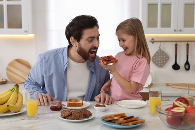 Father and his cute little daughter having fun during breakfast at table in kitchen