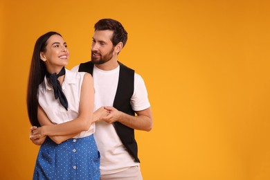 Photo of Happy couple dancing together on orange background, space for text