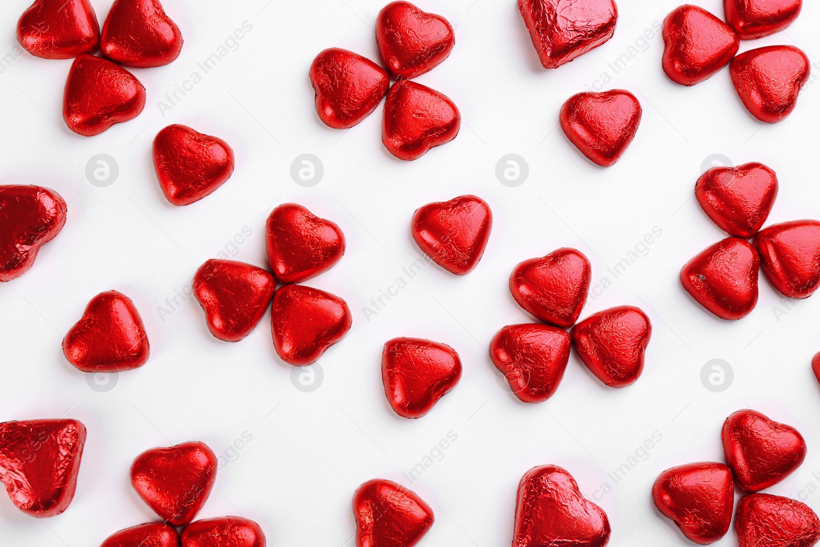 Photo of Heart shaped chocolate candies in red foil on white background, top view