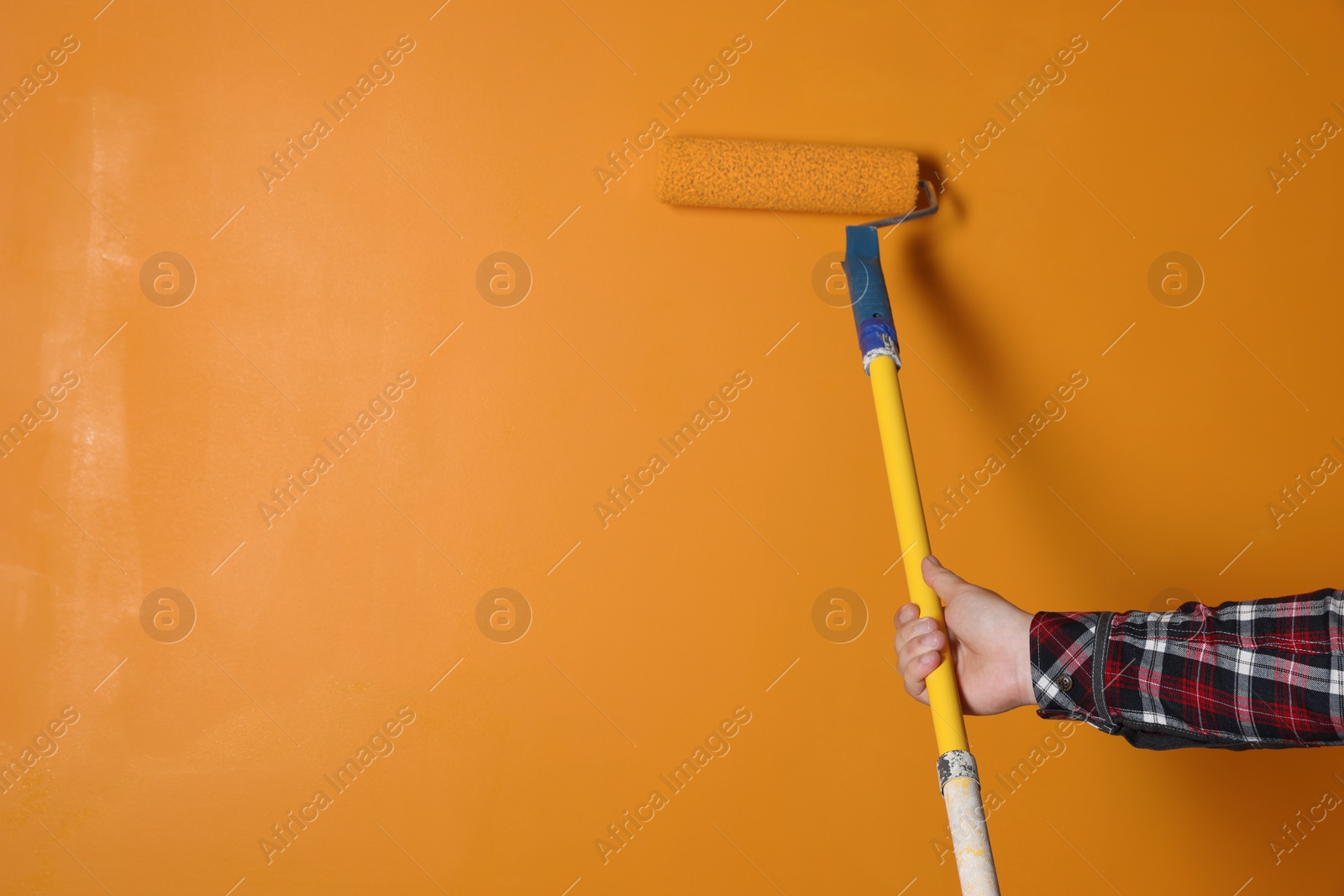 Photo of Man painting wall with roller in orange color, closeup