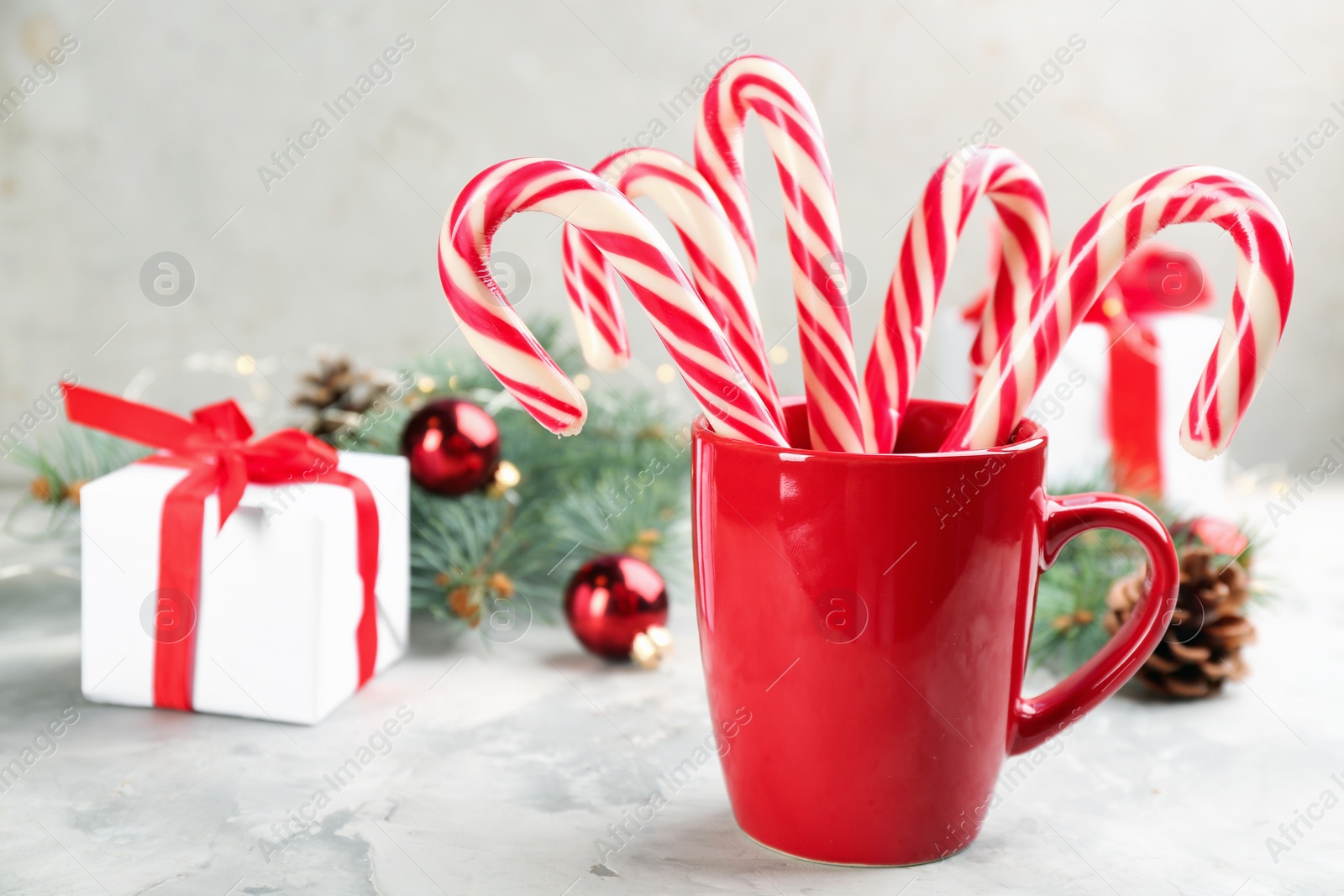 Photo of Many sweet candy canes, gift box and Christmas decor on light table. Space for text