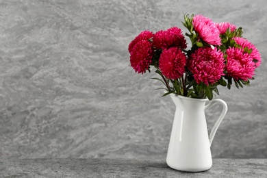 Photo of Beautiful pink asters in jug on table against grey background, space for text. Autumn flowers