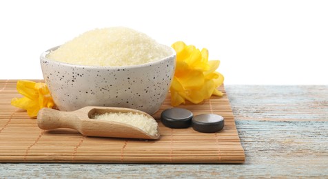 Photo of Natural sea salt in bowl, flowers, spa stones and scoop on wooden table against white background