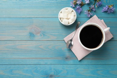 Photo of Cup of delicious chicory drink, sugar and flowers on turquoise wooden table, flat lay. Space for text