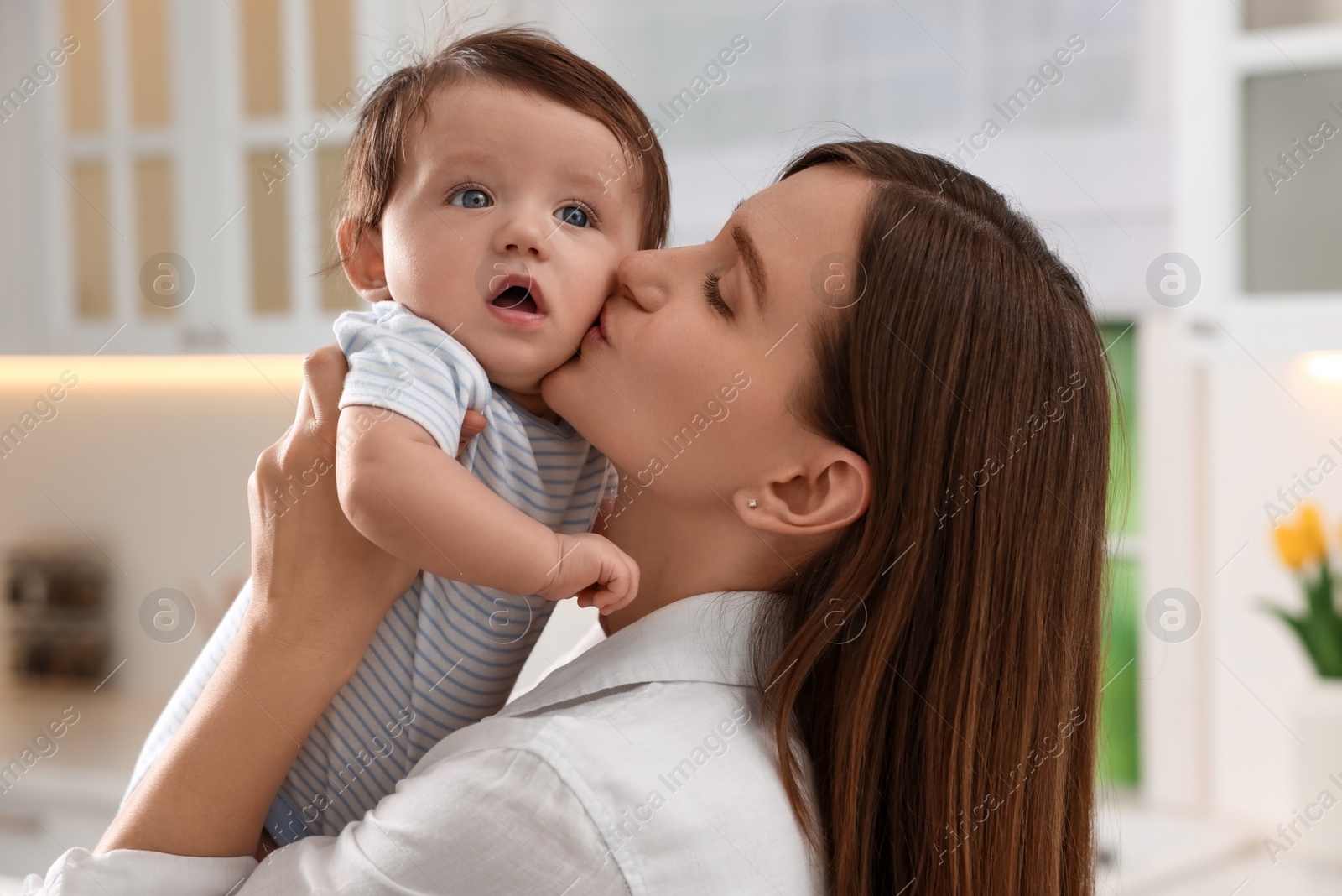 Photo of Happy mother kissing her little baby in kitchen