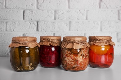 Photo of Many glass jars with different preserved vegetables on light grey table